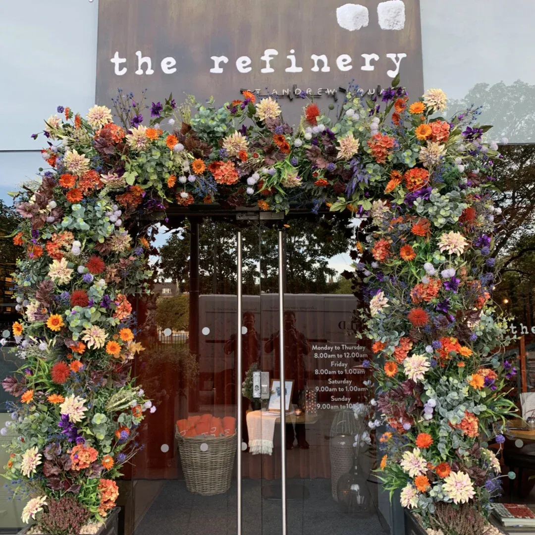 An arch of orange and red flowers over The Refinery's doors