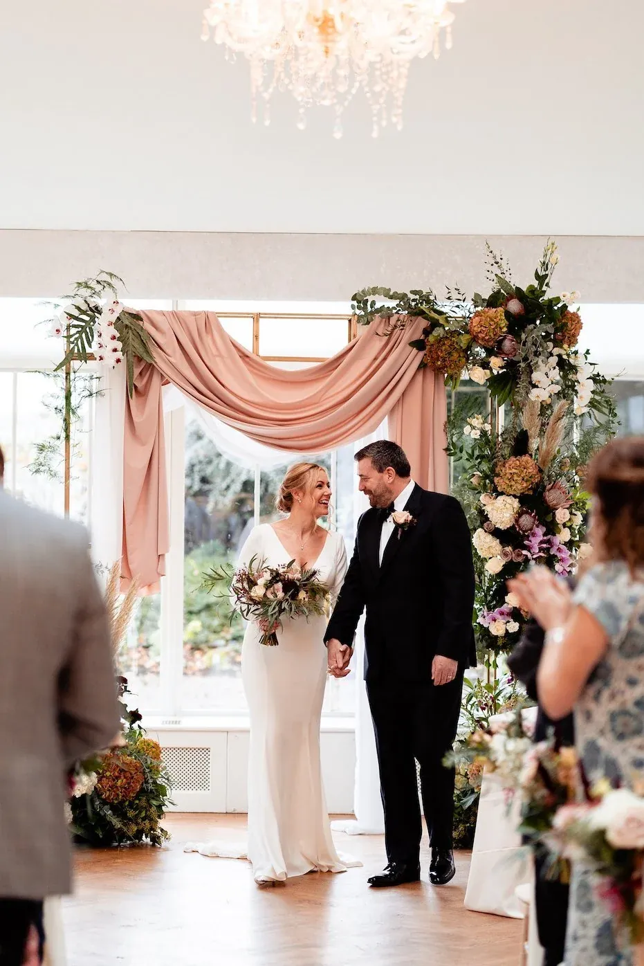A ceremony at Carlowrie Castle under a pink-draped floral arch